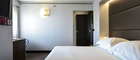 Ett hotellrum med en stor säng, ett skrivbord, en stol, en platt-TV och en dörr.
