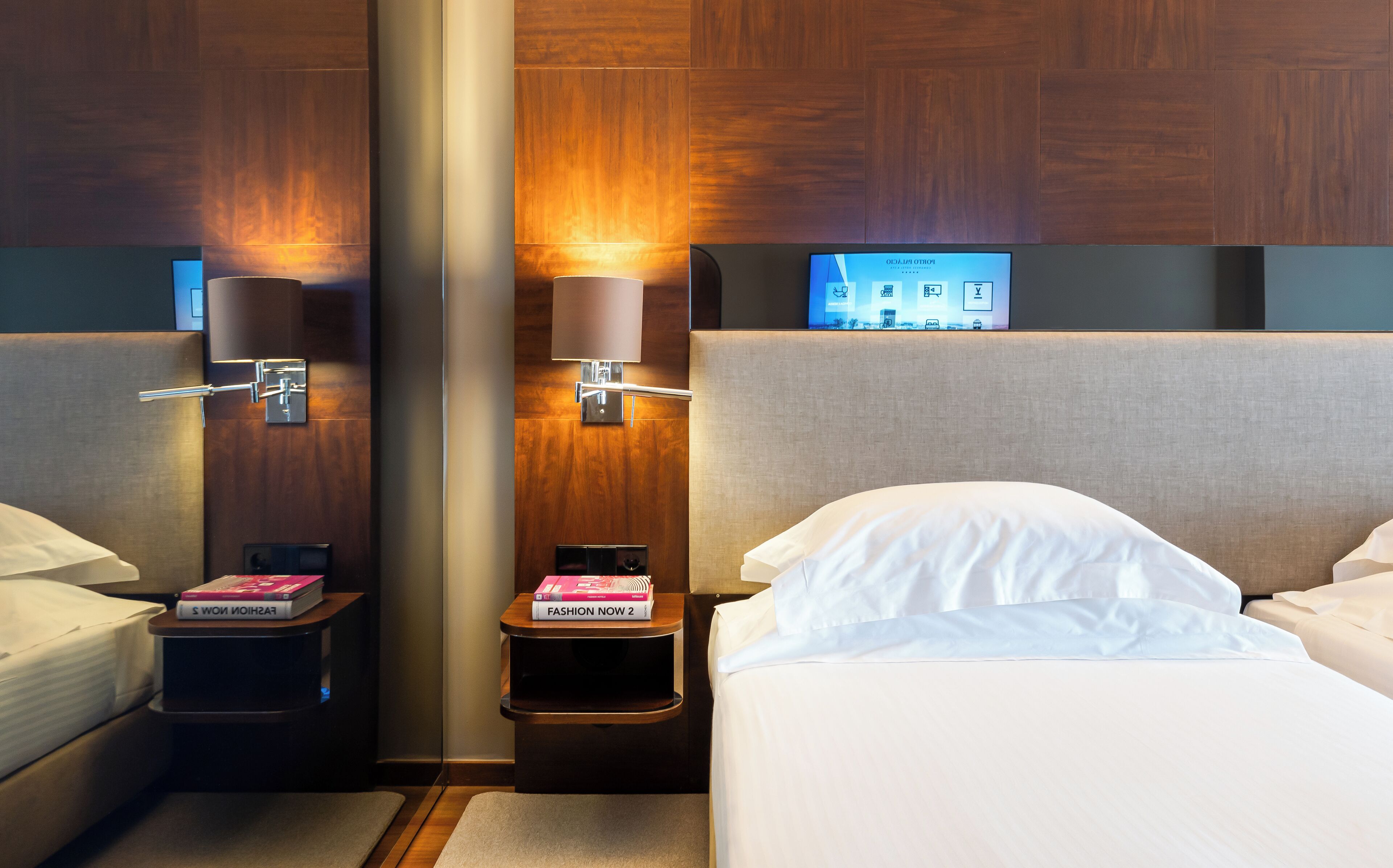 Habitación de hotel con dos camas, una mesita de noche con lámpara, un espejo y un televisor en la pared.