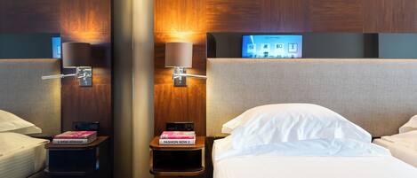 A hotel room with two beds, a nightstand with a lamp, a mirror, and a TV on the wall.