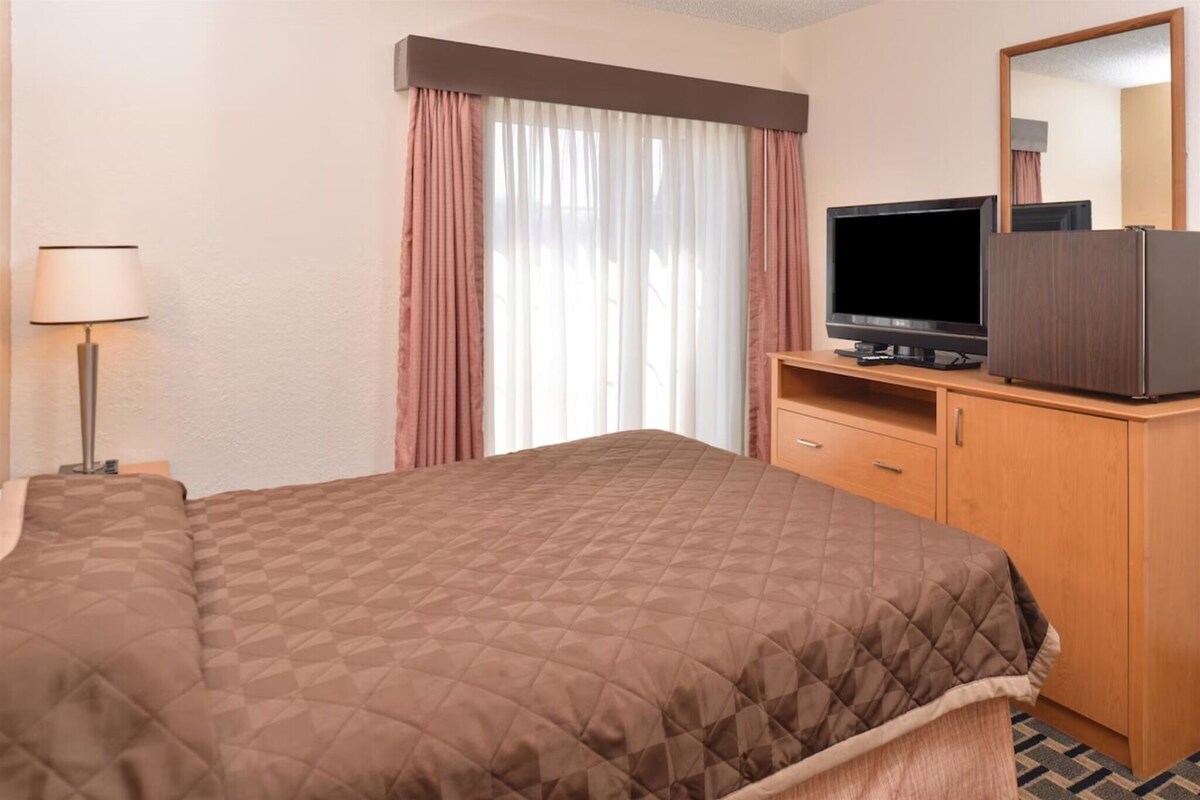 A hotel room with a bed, a television, a dresser, and a window with curtains.