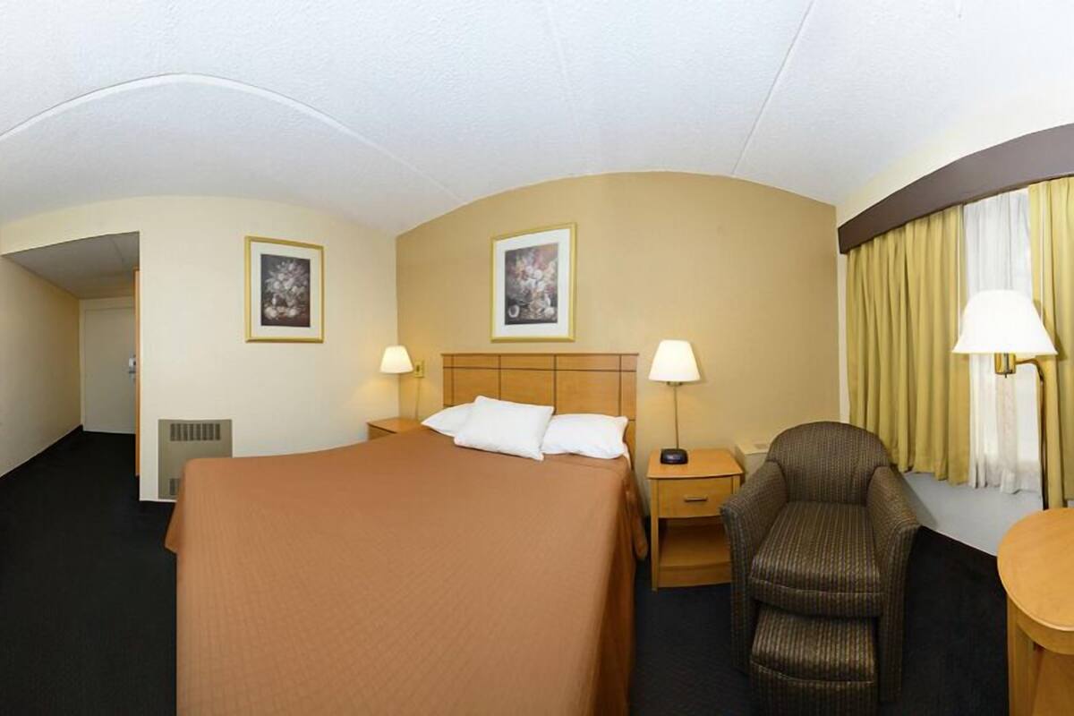 A hotel room with a bed, a TV, a chair, and two lamps.