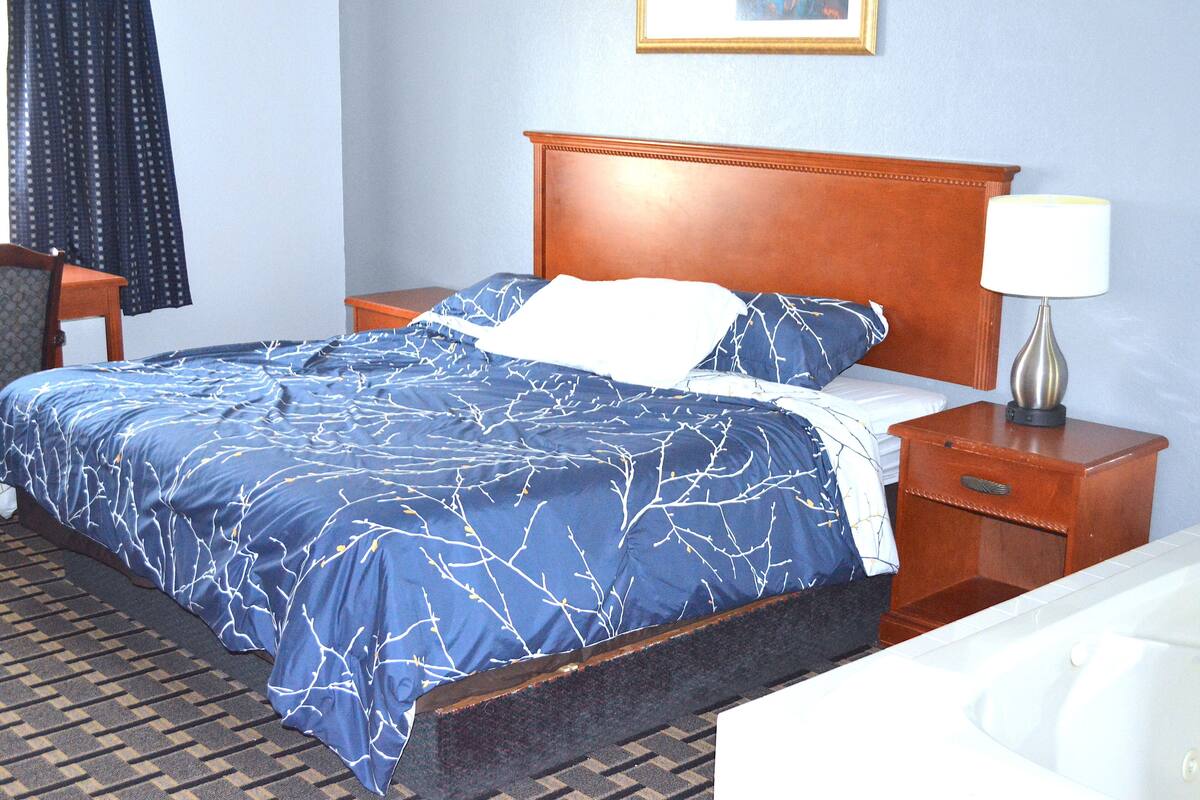 A hotel room with a bed, a nightstand, a lamp, and a chair.