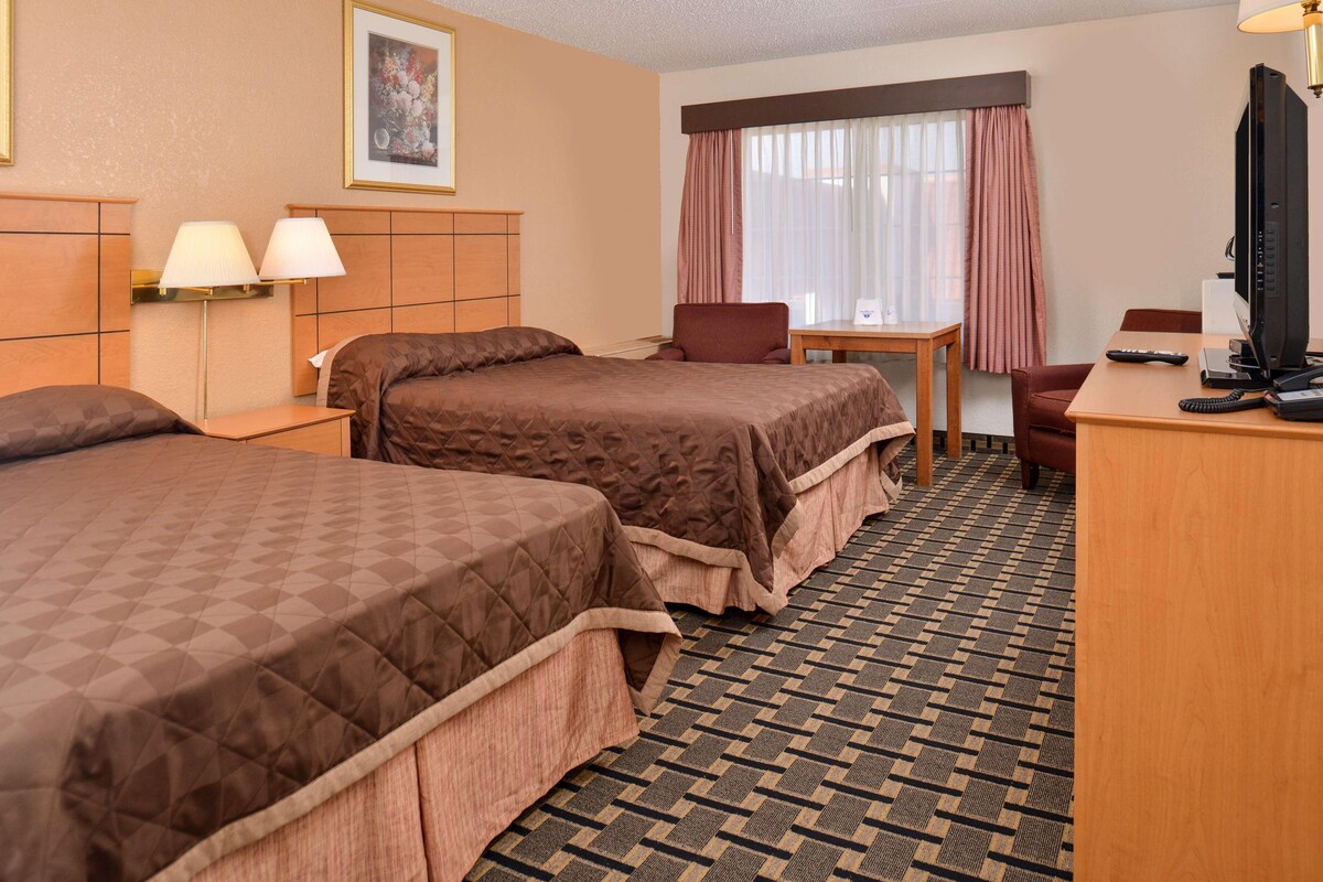 A hotel room with two beds, a desk, a chair, a television, and a window with curtains.