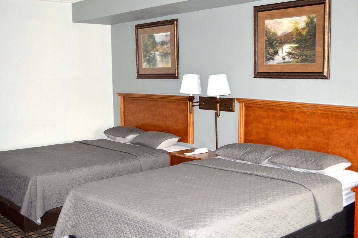 A hotel room with two single beds, a wooden headboard, a nightstand, and two wall-mounted lamps.