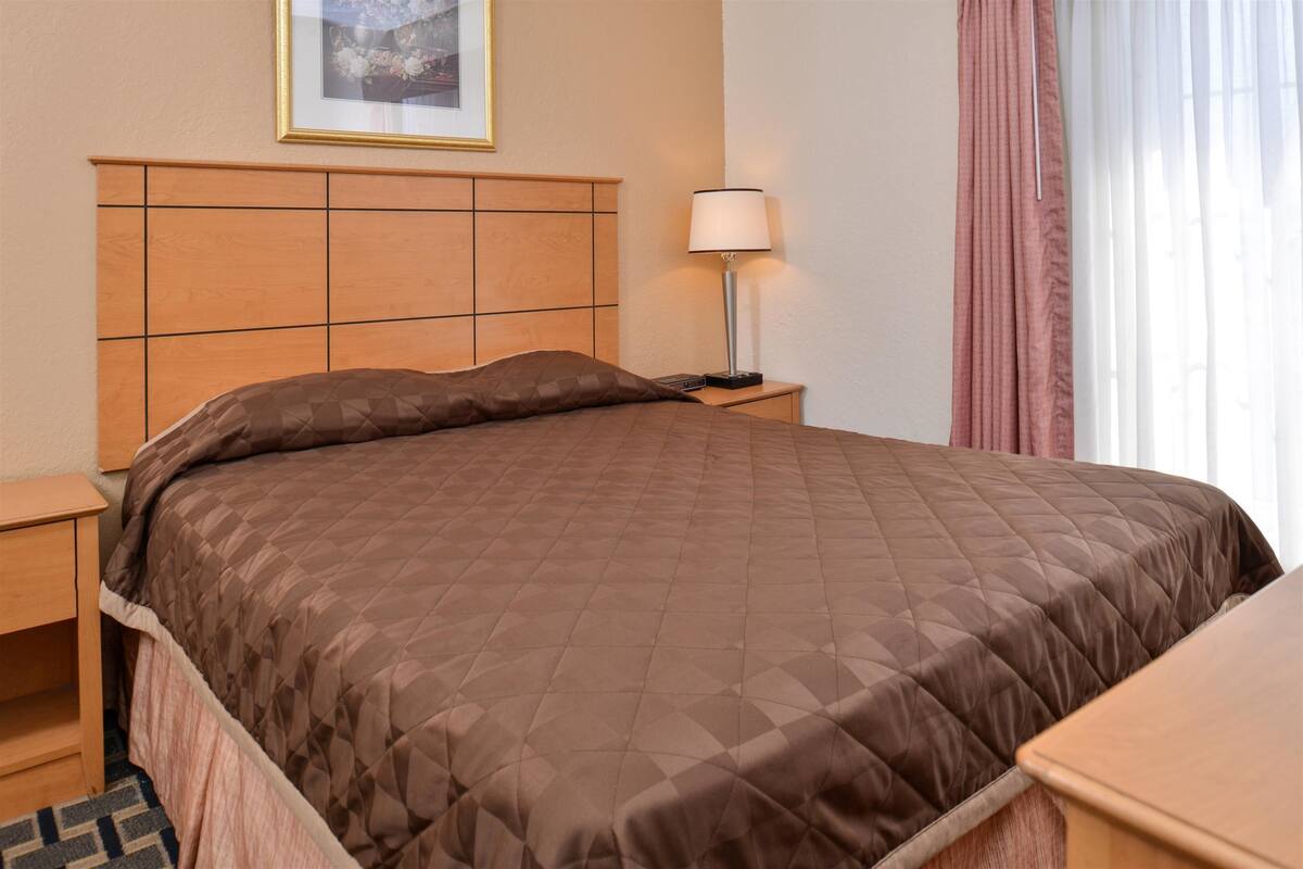 A neatly made bed with a brown quilt, a bedside lamp, and a framed picture on the wall.
