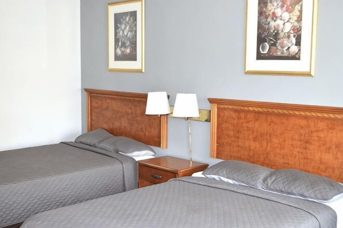 A hotel room with two beds, a nightstand with lamps, and framed artwork on the walls.