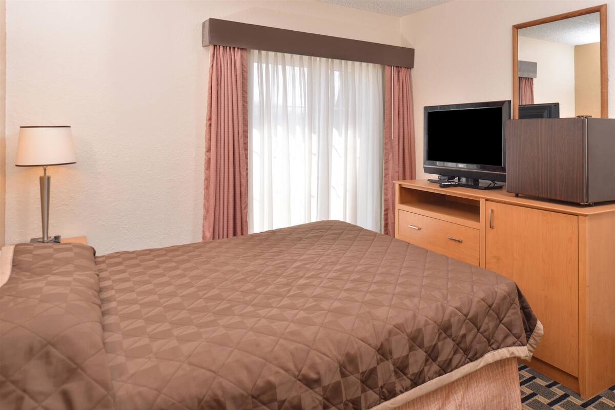 A hotel room with a large bed, a television, a wooden dresser, and a lamp.