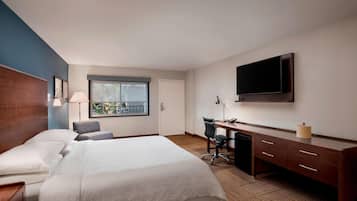 Ett hotellrum med en säng, ett skrivbord, en stol och en tv.