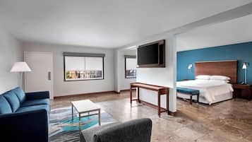 A modern hotel room with a bed, a sofa, a TV, and a desk.