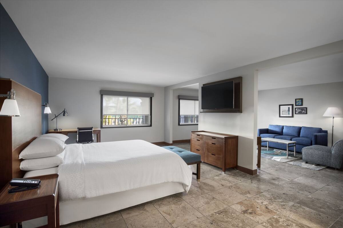 A modern hotel room with a large bed, a desk, a sofa, and a TV mounted on the wall.
