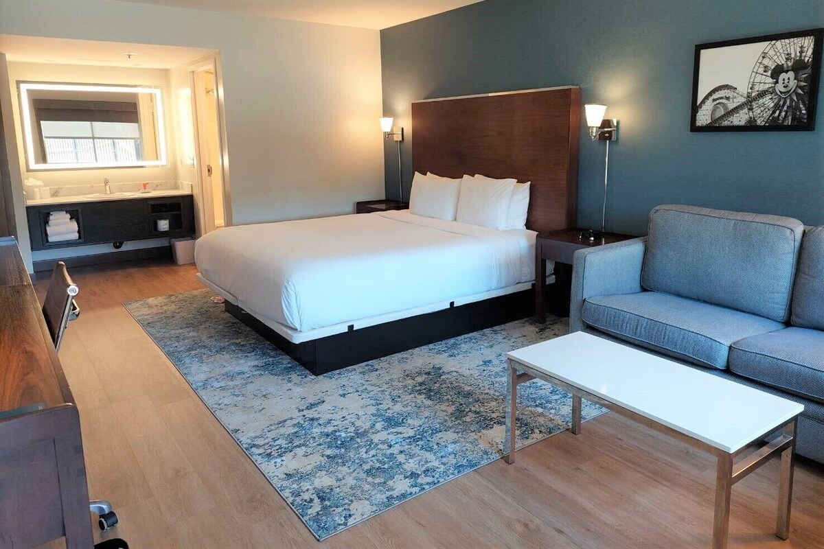 Une chambre d’hôtel moderne dotée d’un grand lit, d’un canapé, d’une petite table et d’une salle de bain avec un meuble-lavabo et un miroir.