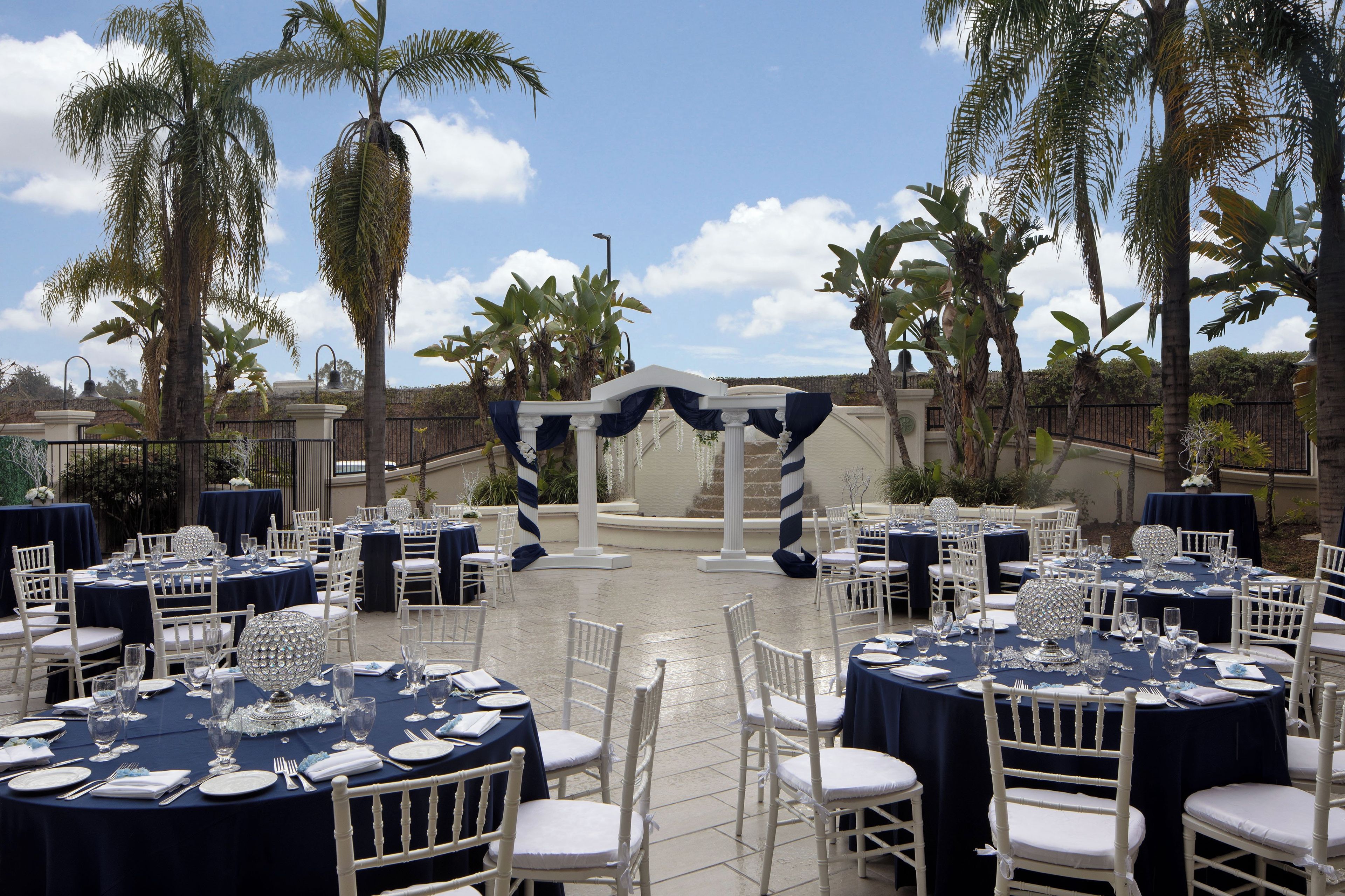 An outdoor wedding venue with round tables, white chairs, and a central archway.