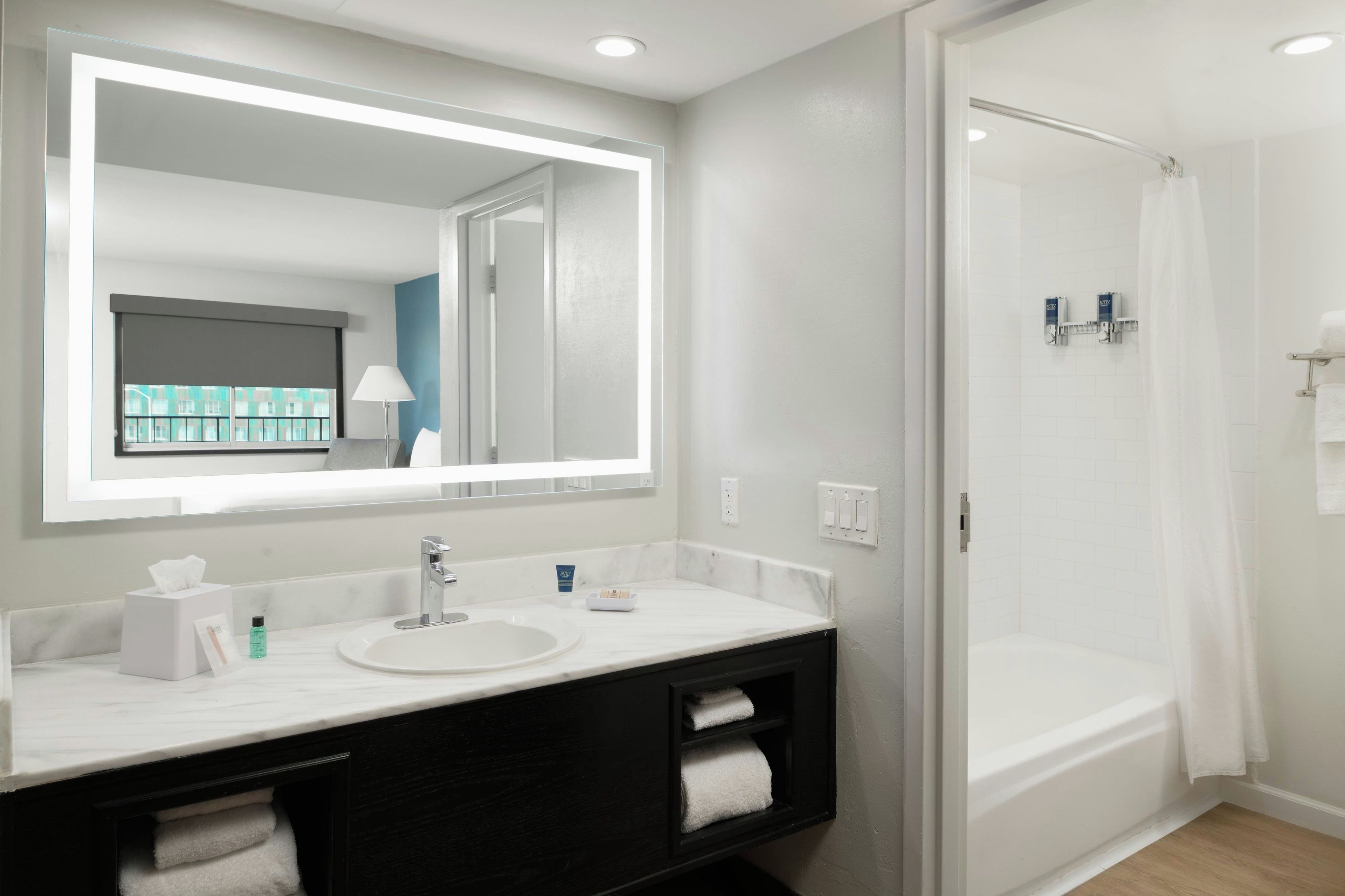 A modern bathroom with a large mirror, a sink, a black vanity, and a shower.