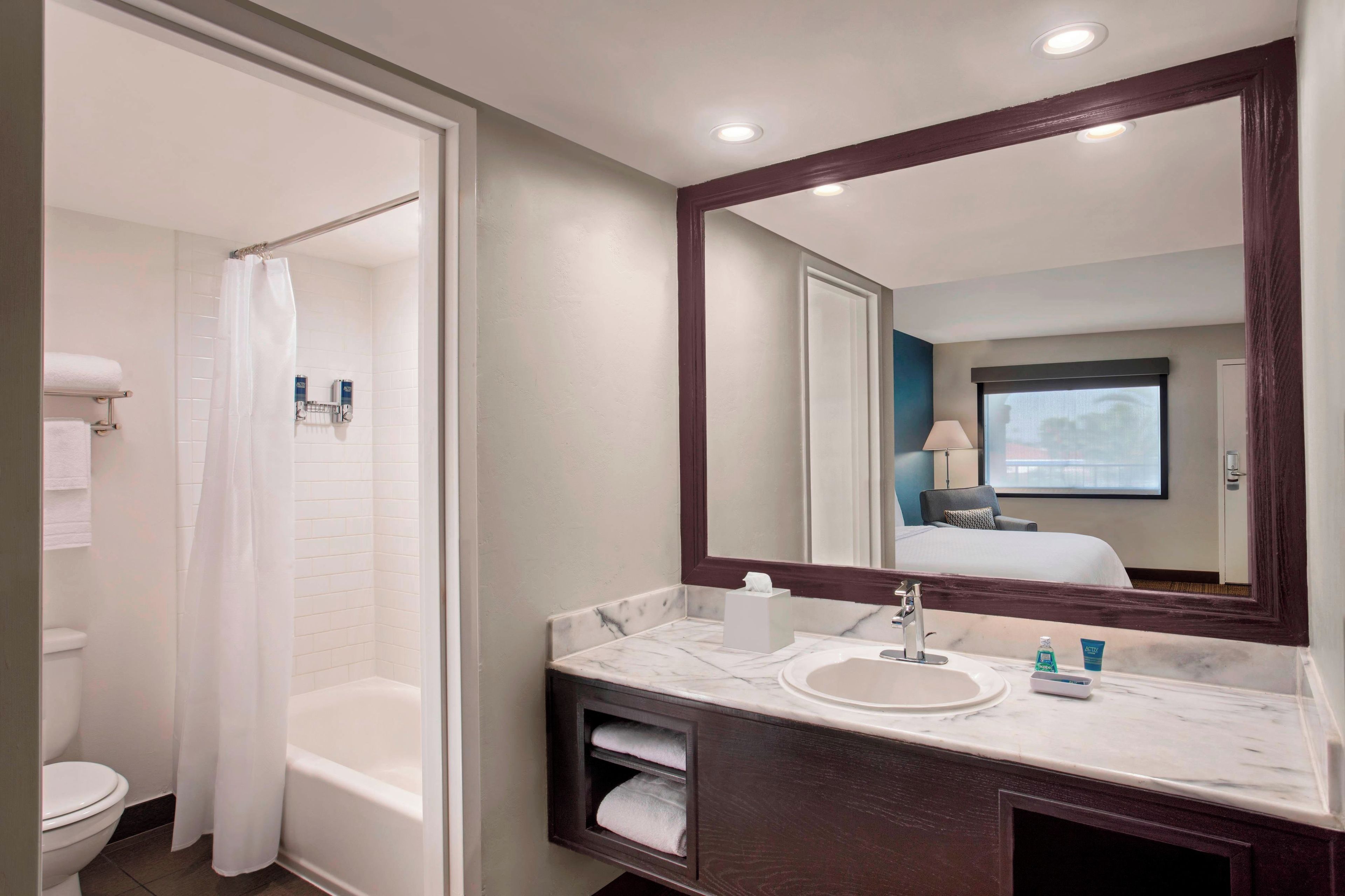 A hotel bathroom with a bathtub, a sink, a mirror, and a shower curtain.