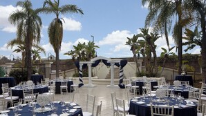 An outdoor dining area with round tables, white chairs, and blue tablecloths. - Four Points by Sheraton Anaheim (Anaheim)