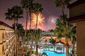 A hotel with a pool, palm trees, and fireworks in the background. - Four Points by Sheraton Anaheim (Anaheim)