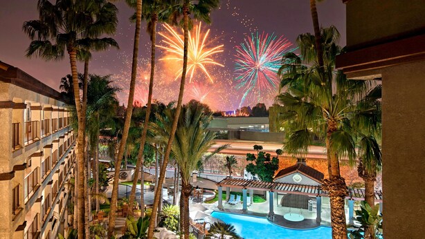 A hotel with a pool, palm trees, and fireworks in the background. - Four Points by Sheraton Anaheim (Anaheim)