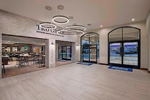 Un espacio interior amplio con cocina moderna de estilo americano y asiático, y un bar de cerveza artesanal, grandes ventanales que ofrecen vistas, y suelo de madera.