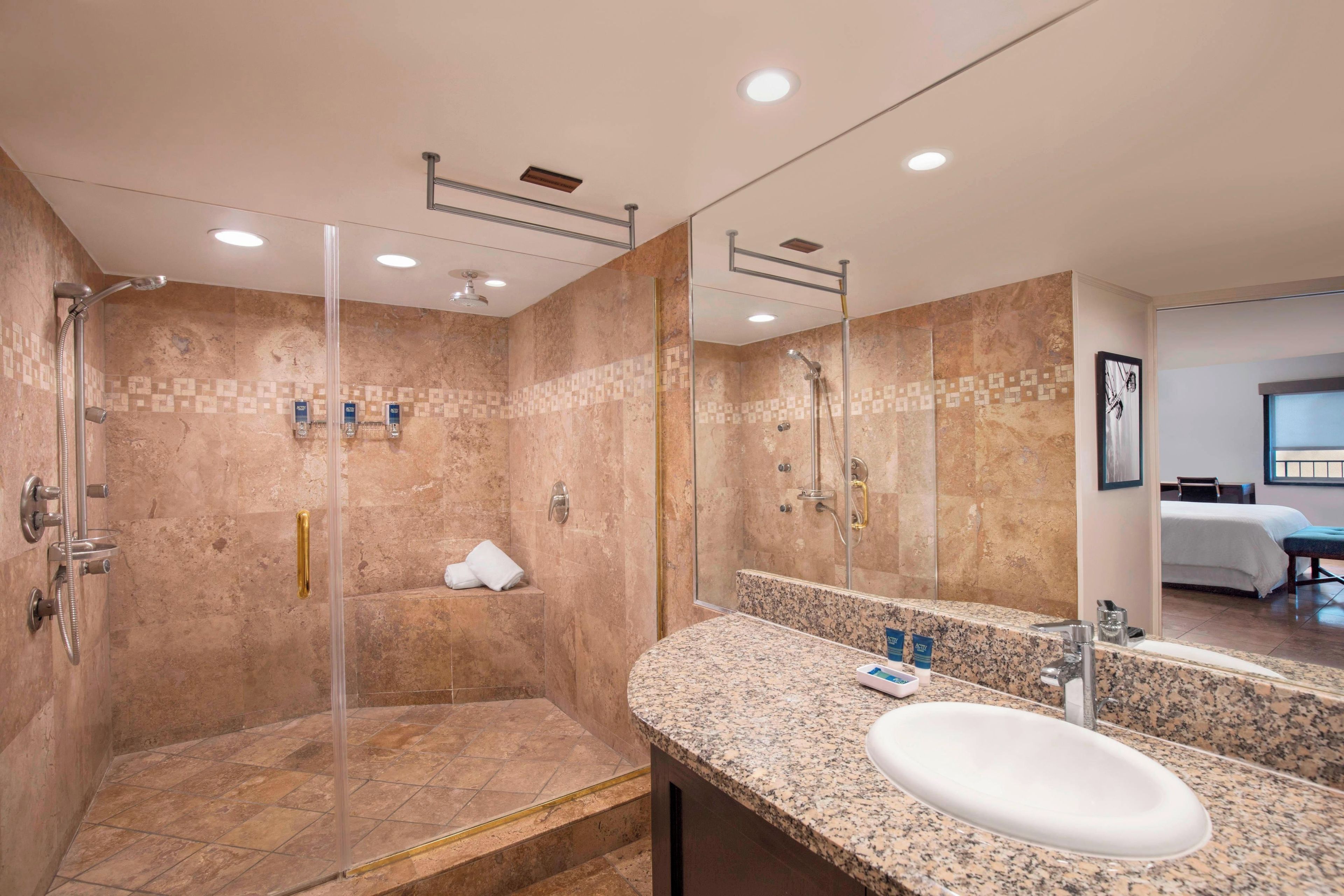 Un baño moderno con cabina de ducha de vidrio, encimera de granito y un espejo grande.