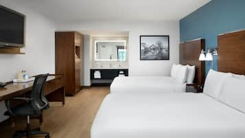 A hotel room with two beds, a desk, a chair, a TV, a bathroom with a mirror, and a painting on the wall.