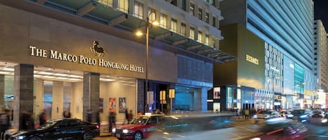 A hotel facade with signage for 'The Marco Polo Hong Kong Hotel' and 'Hermes' across the street.