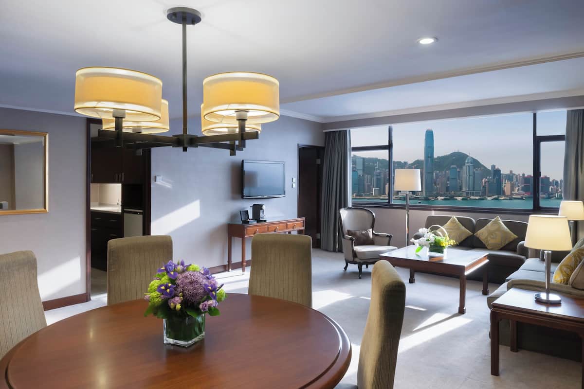 A hotel room with a dining table, chairs, a sofa, a TV, and a view of a cityscape.