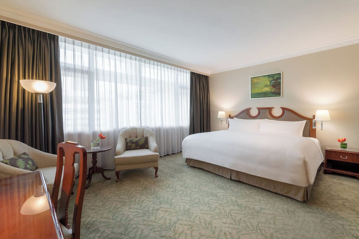 A hotel room with a large bed, a chair, a desk, and a window with curtains.