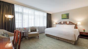 A hotel room with a large bed, a chair, a desk, and a window with curtains.