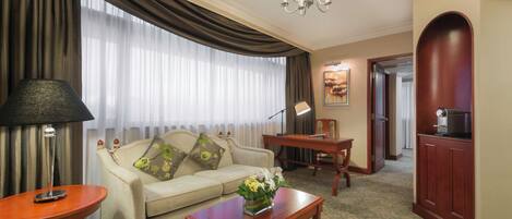 A hotel room with a sofa, a coffee table with flowers, a lamp, a TV, and a chandelier.
