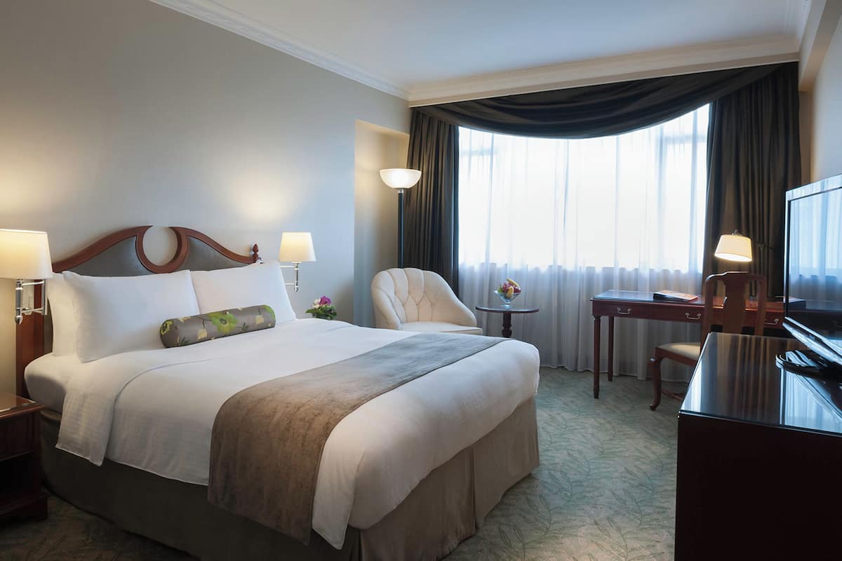 A hotel room with a large bed, a desk, a chair, a television, and a window with curtains.