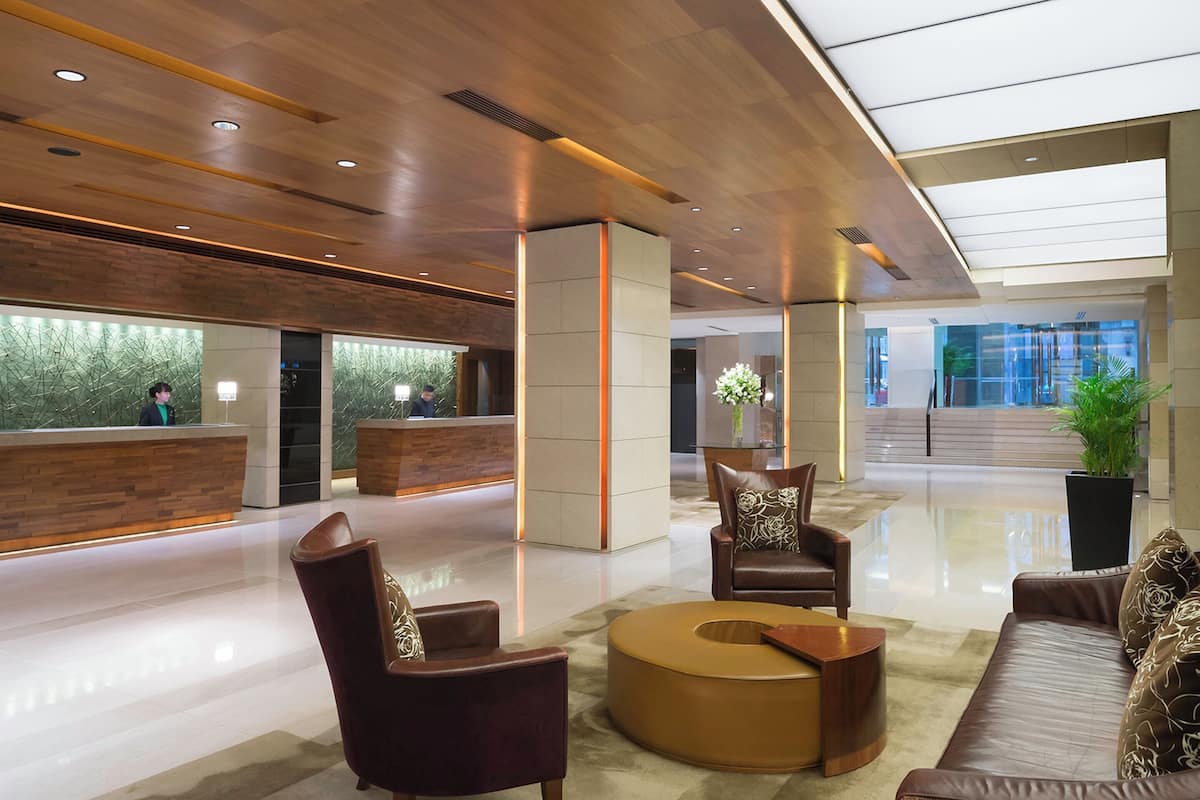 A modern lobby with a reception desk, leather seating, a coffee table, and a large potted plant.