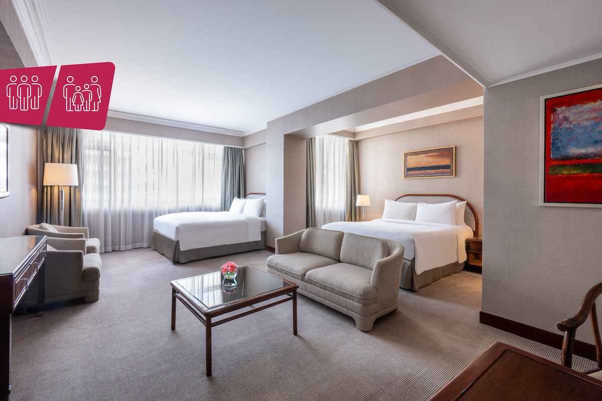 A hotel room with two beds, a sofa, a coffee table, and a desk.