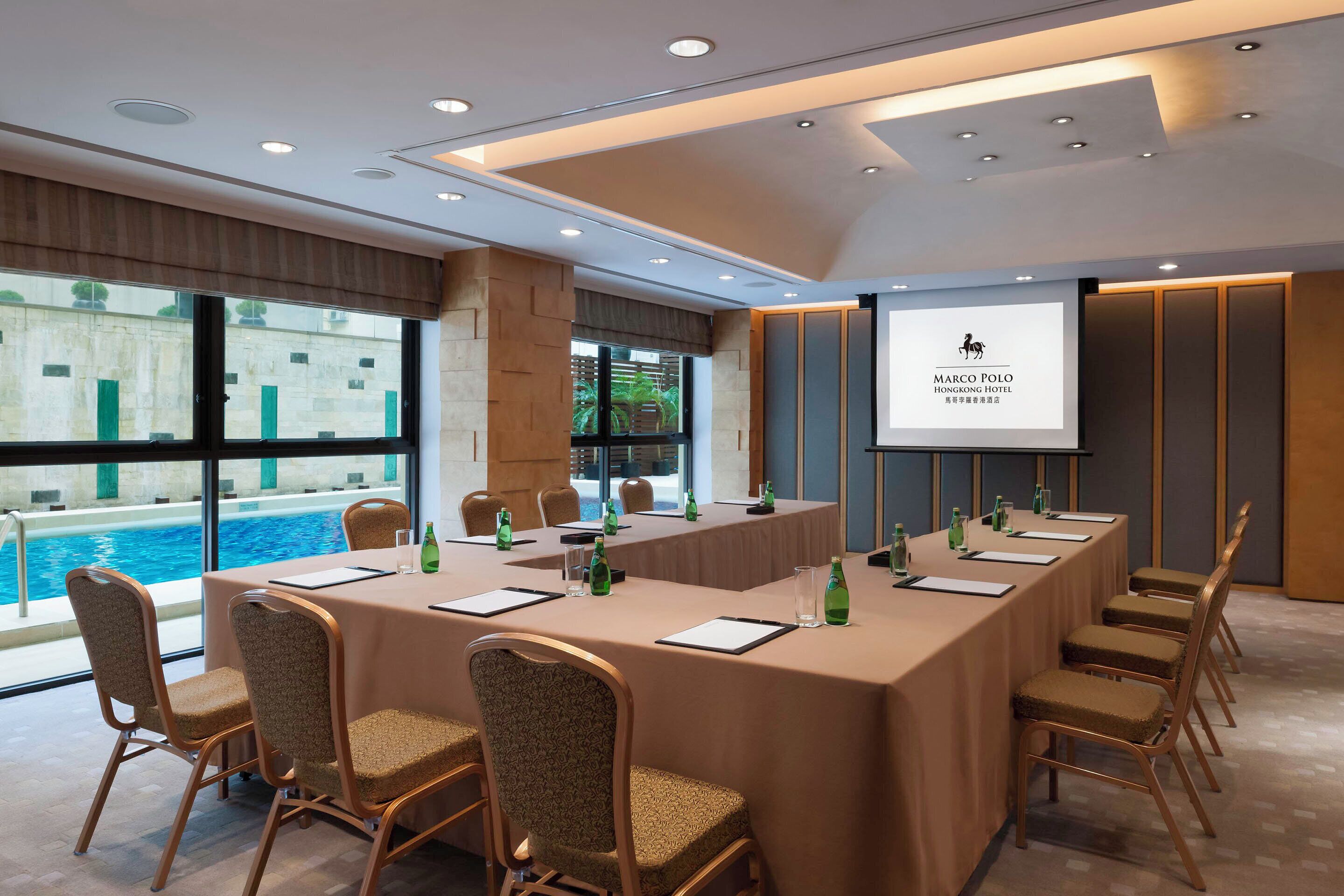 A conference room with a long table, chairs, and a projector screen displaying the hotel name.