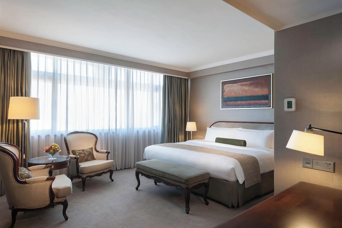 A hotel room with a large bed, two armchairs, a small table with a lamp, and a painting on the wall.