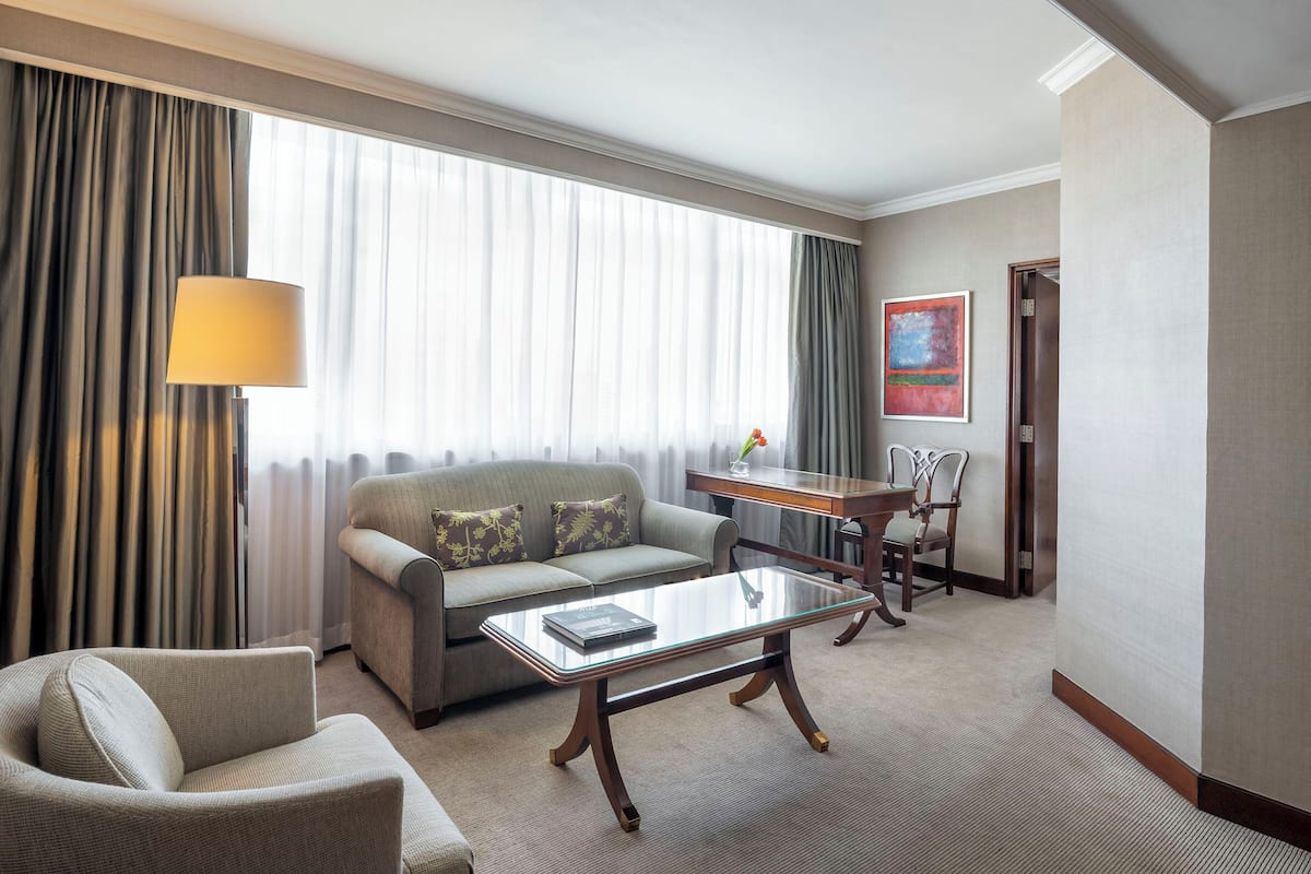 A hotel room with a sofa, armchair, coffee table, and a desk with chairs.