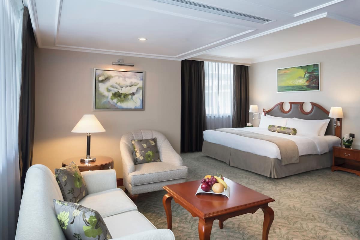 A hotel room with a bed, a sofa, a chair, a table with fruit, and two lamps.