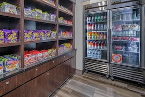 A snack and beverage vending area with multiple shelves stocked with various snacks and a refrigerator with beverages. - Holiday Inn Express & Suites Anaheim Convention Center Area by IHG (Anaheim)
