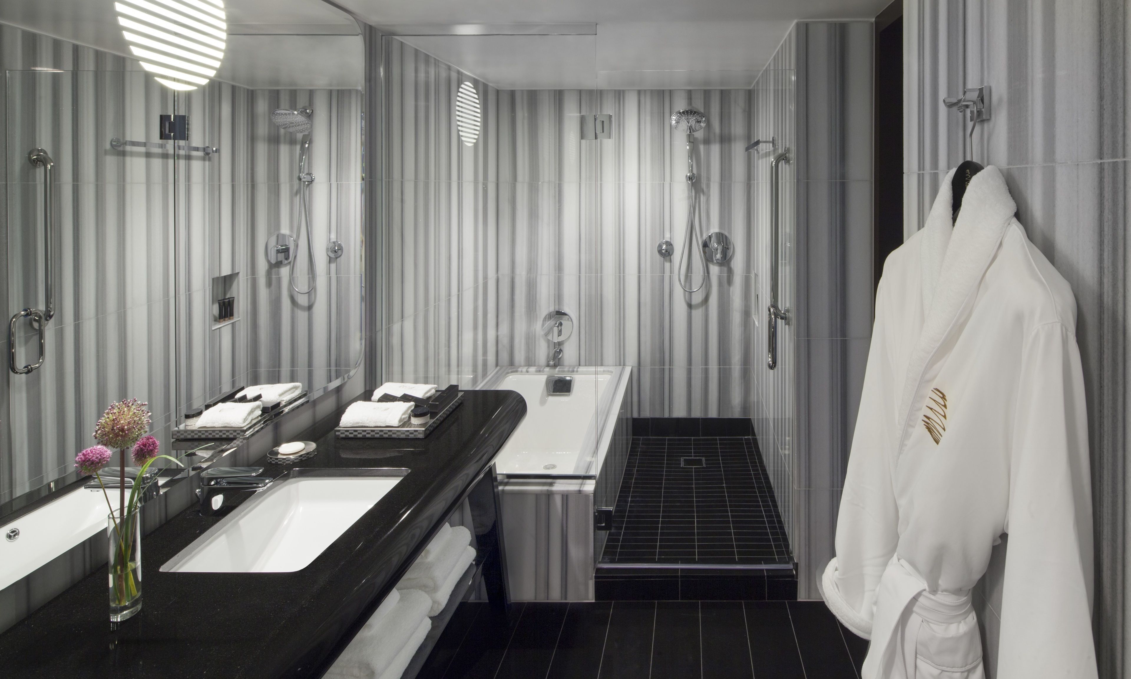 A modern bathroom with a large mirror, a black sink, a white bathtub, and a shower area.
