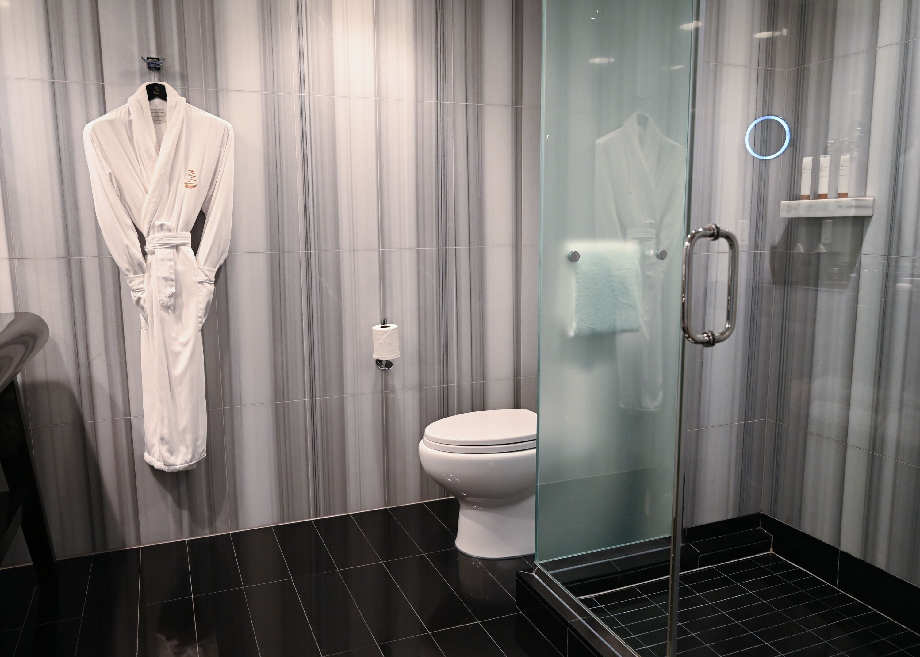 Ein modernes Badezimmer mit Duschkabine aus Glas, einer weißen Toilette und einem Bademantel, der an der Wand hängt.