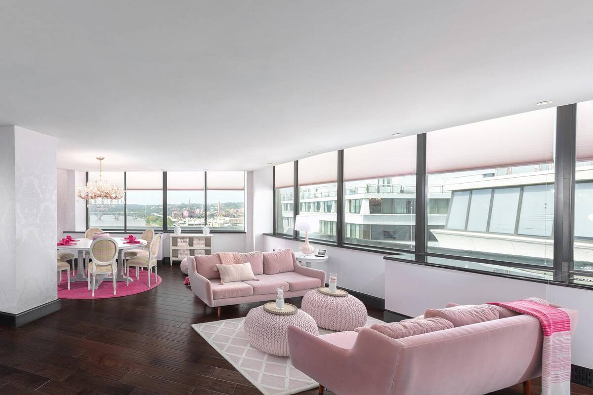 Un salon moderne doté d’une grande fenêtre, d’un coin repas et d’un ensemble de canapés rose.