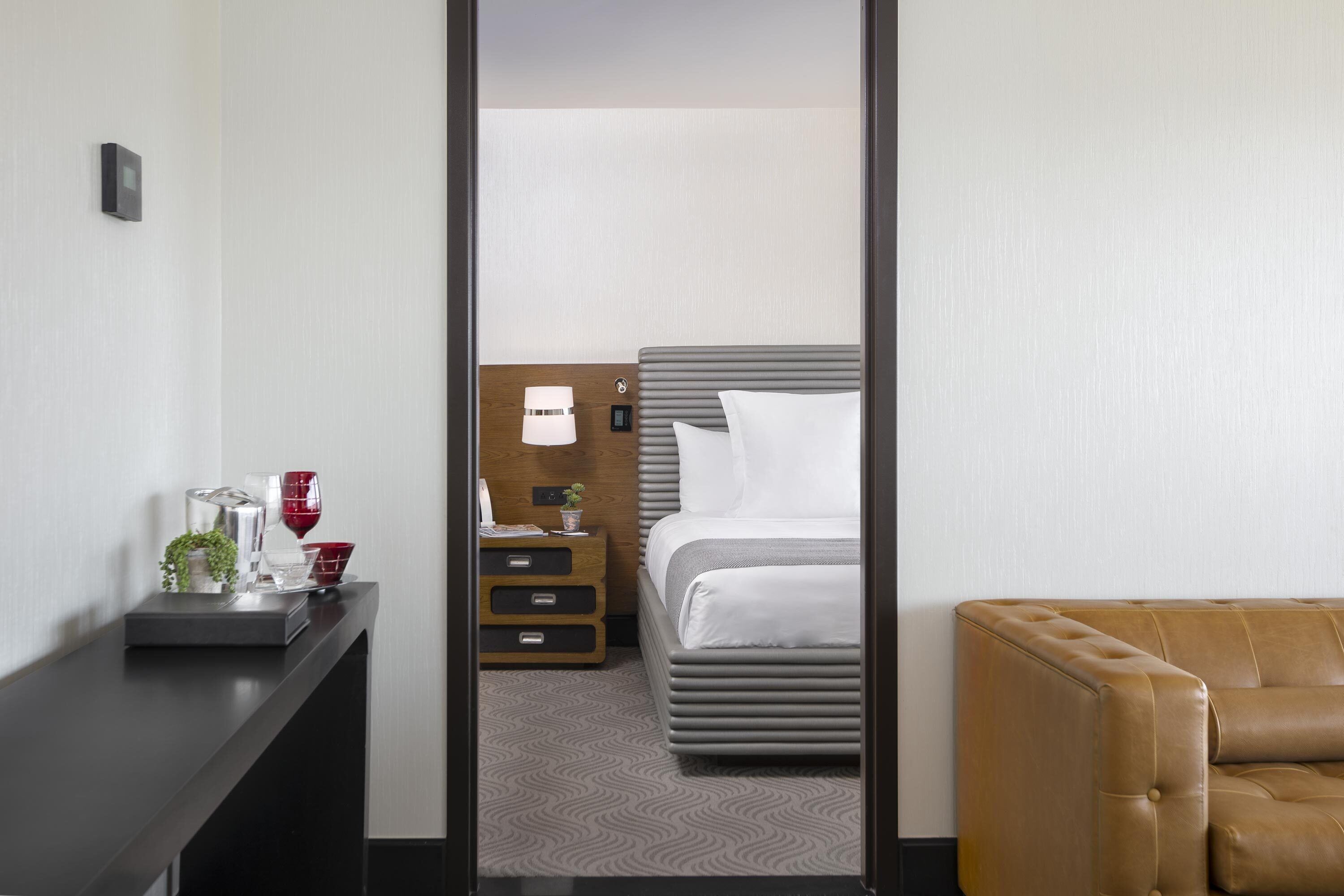 A hotel room with a bed, bedside table, and a brown leather sofa.