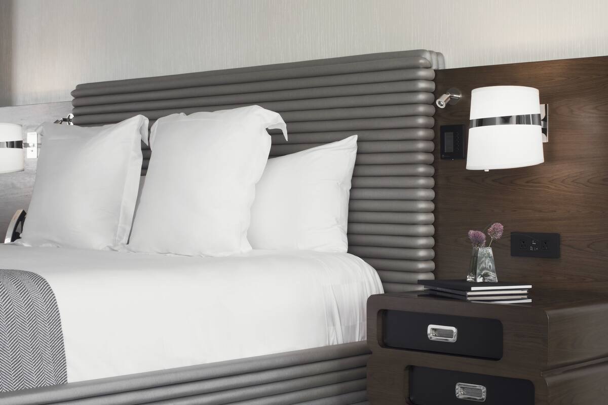 Une chambre d’hôtel moderne avec un grand lit, une table de chevet avec une lampe et une tête de lit en bois.