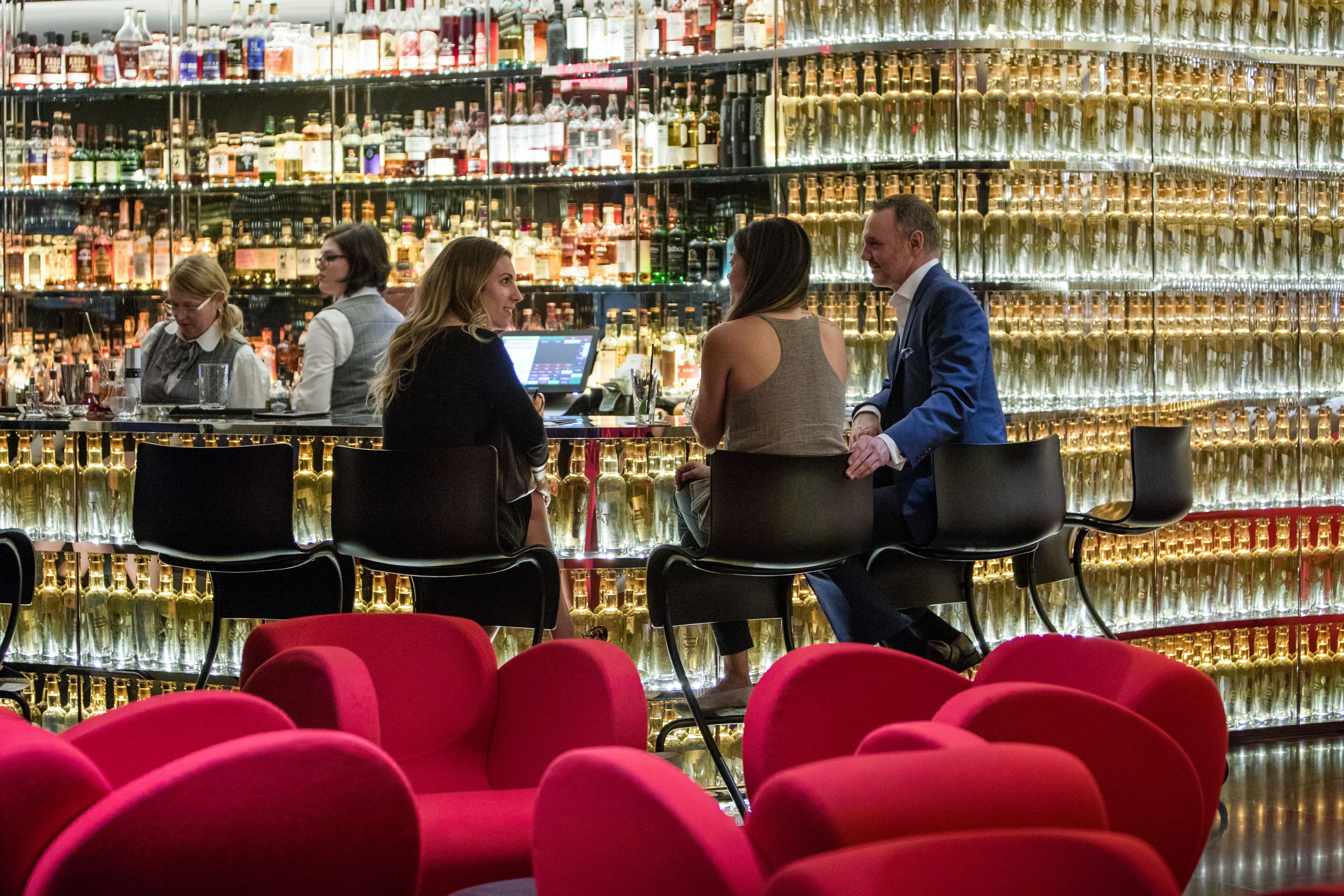 A bar with multiple shelves of liquor bottles, bar stools, and a counter with a computer.