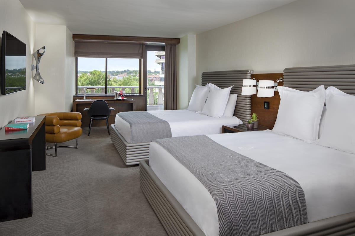 Une chambre d’hôtel avec deux lits, un bureau, une chaise et une vue sur la ville.