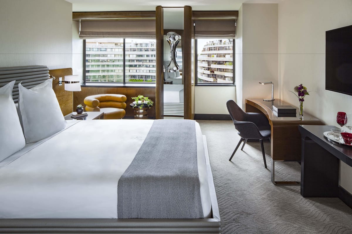 Une chambre d’hôtel moderne, dotée d’un grand lit, d’un bureau et offrant une vue sur le paysage urbain.