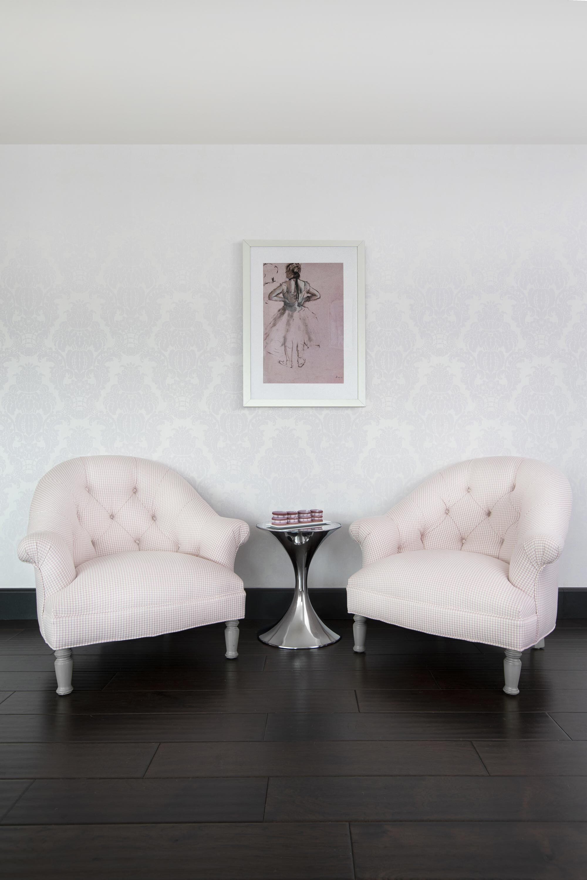 A room with two upholstered chairs, a small round table, and a framed picture on the wall.