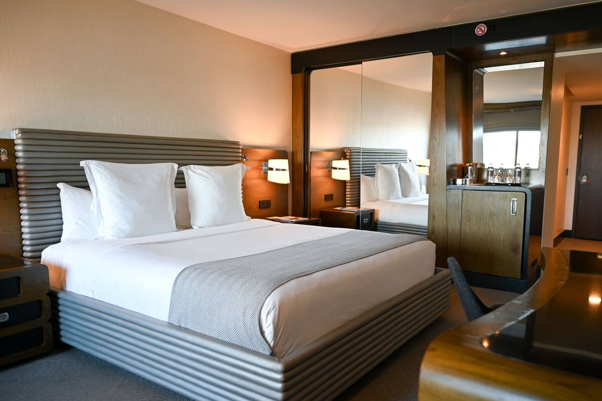 Une chambre d’hôtel avec un grand lit, une table de chevet, un miroir et un bureau en bois.