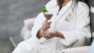 A person in a white bathrobe holding a martini glass with a mint garnish.