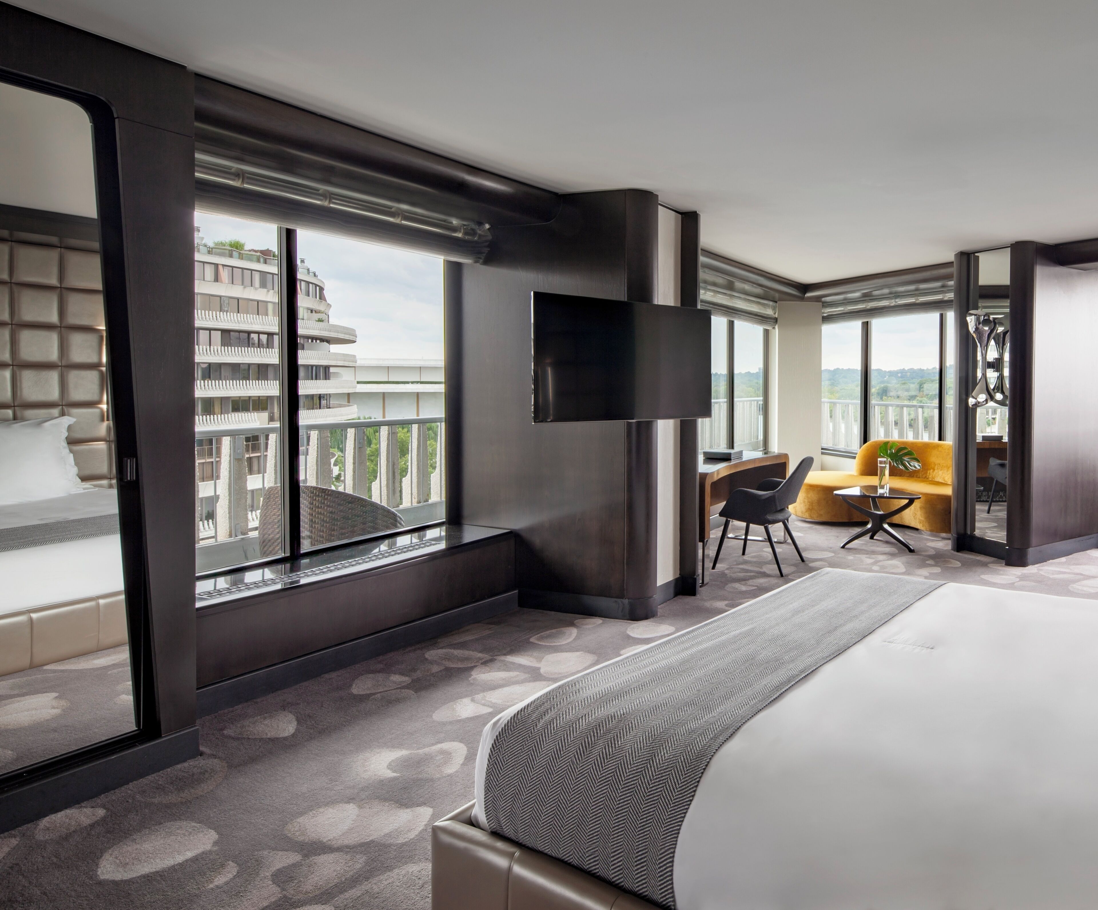 Habitación de hotel moderna con una cama grande, televisión, sofá y balcón con vistas a la ciudad.