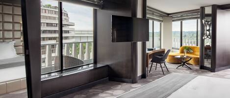Habitación de hotel moderna con una cama grande, televisión, sofá y balcón con vistas a la ciudad.